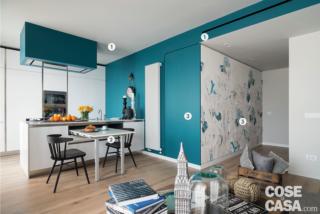 Tra l'ingresso e la zona giorno, la tappezzeria floreale su fondo bianco è di LondonArt, mentre la pittura blu petrolio usata per tinteggiare l'altra parete è di Covema. Le sedie in faggio verniciato nero vicino al tavolo estraibile sono di Dialma Brown. Il parquet in listoni di rovere provenzale, posato in tutta la casa, è di Itlas. In tutta la casa, l'impianto di climatizzazione canalizzato è di Cobram.