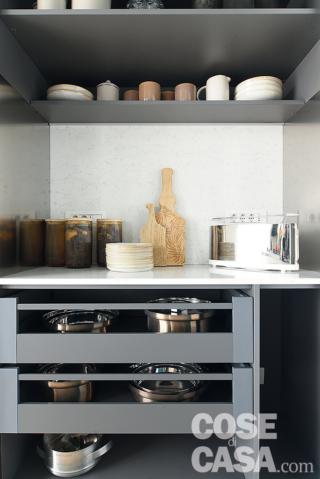 In cucina la composizione è realizzata su misura dal falegname con frontali in laminato bianco; gole, dettagli ed estetica degli elettrodomestici sono in acciaio inox. Incassata in un volume a isola in cartongesso tinteggiato color petrolio come la parete, la cappa è di Faber. Le zone cottura e lavaggio sono incassate nella penisola; un altro piano di lavoro è chiuso dietro le ante dell'armadio sulla destra lungo la parete.
