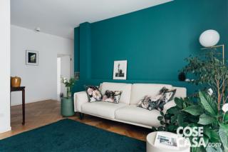 soggiorno dell'appartamento ristrutturato, zona conversazione, parete color ottanio, divano in tessuto bianco, lampada a sfera di design, parquet, tappeto blu, tavolino, piante da appartamento, controsoffitto, faretti