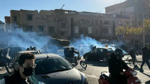 EPA A cloud of tear gas floats across a road as cars and motorcycles pass through it, in Tehran (25/12/25)