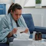 Person with disease infection analyzing package leaflet of pill bottles to cure illness. Woman feeling cold reading medical paper with medication instructions, having medicaments on table