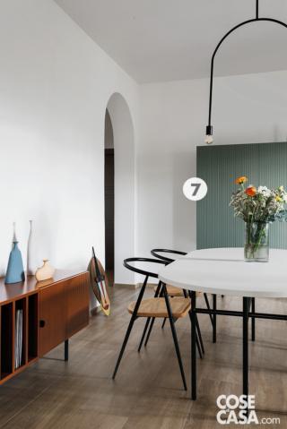 Nell'ambiente aperto della zona giorno, il tavolo da pranzo è di fronte alla vetrata che lascia a vista la cucina, disposta in un locale indipendente. Il mobile tv basso con frontali listellati che, lungo la parete, raccorda le diverse aree del living, è su disegno dei progettisti, così come la credenza sull'altro lato e il tavolo con piano in laminato Fenix. Le sedie, con seduta in paglia di Vienna e struttura in ferro, fanno pensare a una rivisitazione attualizzata della classiche Thonet. La sospensione asimmetrica, sempre in ferro, è stata realizzata dal fabbro mentre l'applique in resina a forma di scimmia nell'angolo è il modello Monkey Lamp di Seletti. Le ceramiche artigianali appoggiate sul piano sono di Giorgio Di Palma.